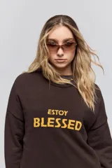 Sweater de punto marrón de tejido liviano y calce relajado, con hombros caídos, cuello redondo y puños y cintura en rib. Cuenta con una estampa tejida en el frente con la frase "Estoy Blessed" en color amarillo.