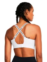 Top deportivo Under Armour de sujeción media, color blanco, con tirantes ajustables que incluyen el logo de la marca y banda elástica inferior con logo central. Cuenta con paneles laterales de malla para ventilación y relleno moldeado.