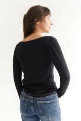 Remera básica de manga larga en color gris melange, confeccionada en algodón suave. Presenta un diseño de cuello redondo y un detalle de etiqueta decorativa en el puño.