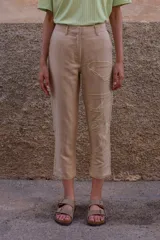 Pantalón chino color beige de lino y viscosa, con bordado de palmeras en verde claro. Tiene tiro medio-alto, pierna recta y bolsillos laterales y traseros.