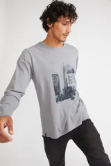 Remera de manga larga color gris melange, con cuello redondo y estampado gráfico en blanco y negro de la ciudad de Nueva York en el frente.