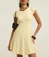 Vestido corto color amarillo pálido, con escote redondo y mangas cortas. Presenta recortes verticales en el torso que definen la silueta y una falda ligeramente acampanada.