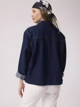 Chaqueta de jean azul oscuro con cierre frontal con lazos, mangas 3/4 con puños doblados, bolsillos de parche en el frente y corte holgado.