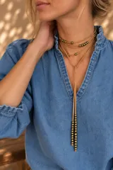 Collar estilo corbatín de tiento de cuero color tostado, con múltiples vueltas al cuello y detalles de cuentas metálicas doradas en el cordón y en los extremos.