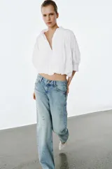 Camisa de algodón con cuello solapa, mangas abullonadas por debajo del codo y bajo acabado en globo. Presenta cierre frontal con botones ocultos.