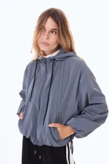 Campera impermeable corta con capucha, cierre frontal y cordones ajustables. Presenta un diseño holgado con mangas amplias y puños elásticos.