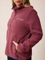 Canguro de sherpa color bordó, con cuello alto y cierre frontal parcial. Presenta un bolsillo con cierre en el pecho y bolsillos laterales, confeccionado en tejido de textura suave y abrigada.