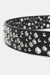 Cinturón de efecto piel en color negro, con diseño de tachas metálicas y perforaciones decorativas a lo largo de toda la pieza. Cuenta con hebilla metálica cuadrada en tono plateado.
