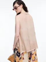 Camisa sin mangas color beige claro con efecto teñido en frío y aspecto gastado. Presenta cuello clásico, cartera oculta y ruedo irregular, más largo en los laterales.