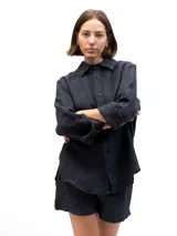 Camisa de lino de corte relajado, color negro, con cuello clásico, cierre frontal de botones y mangas largas con puños doblados.