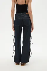 Pantalon de jean azul oscuro de corte ancho y tiro bajo, con detalle de aberturas laterales ajustables mediante lazos.