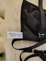 Conjunto de bikini negro con textura acanalada. El corpiño es de corte triangular con breteles regulables y detalle de aro metálico en el centro. La bombacha es tipo colaless con tiras finas regulables en los laterales.