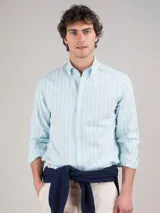 Camisa de hombre de corte regular fit, confeccionada en tejido oxford a rayas verticales celestes y blancas. Tiene cuello button-down, cierre con botones, manga larga con puño simple y logo bordado en el pecho.