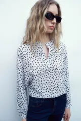 Blusa blanca con estampado floral negro, cuello mao y mangas largas con puños abotonados.