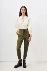 Pantalón tipo babucha de gabardina elastizada, color negro, con cintura elástica ajustable mediante cordón, puños en los tobillos, bolsillos diagonales frontales y bolsillos traseros con solapa y botón.