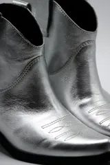 Botas de cuero vacuno color negro con caña baja bordada a tono, tacón bajo, punta alargada redondeada y suela cuadrada.