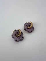 Aros de acero quirúrgico dorado con dije en forma de flor de resina lila con lunares negros.