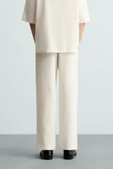 Pantalón de calce relajado confeccionado en tejido de viscosa y yute color tostado. Presenta cintura elástica ajustable con cordón, bolsillos laterales, bolsillos traseros de vivo y cierre frontal con cremallera y botón.