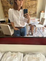 Camisa de estilo romántico confeccionada en tela broderie blanca, con mangas al codo abullonadas y cierre frontal con botones.