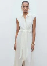 Vestido midi de corte evasé, sin mangas y con cuello camisero. Presenta cierre frontal con botones, un bolsillo de parche en el pecho y un lazo decorativo en la cintura. Confeccionado en tejido con textura de rayas verticales.