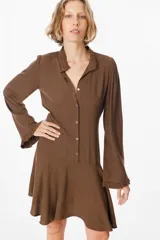 Vestido corto color chocolate, con cuello camisero, cierre frontal de botones y mangas largas con puños con volados. Incluye un lazo ajustable en la cintura y falda con vuelo.