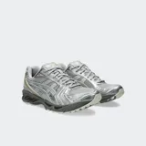 Championes de running Asics modelo Gel Kayano 14, con diseño retro inspirado en los años 2000. Presentan una estructura de malla técnica con superposiciones metálicas plateadas y detalles en gris oscuro, incorporando tecnología GEL en la suela para una amortiguación superior.