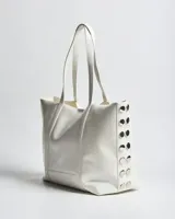 Cartera tipo tote de símil cuero blanco, con dos asas de mano y detalles de herrajes plateados en los laterales.