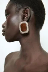 Aros de diseño cuadrado con centro de resina color bordó con vetas oscuras, rodeado por un marco de pequeños cristales brillantes. Cierre con tuerca.
