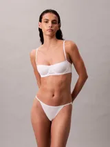 Sujetador tipo balconette Calvin Klein de la línea Cotton Modal Bare, color blanco. Presenta copas suaves sin relleno, aros flexibles para mayor sujeción, tirantes ajustables y cierre de gancho en la parte trasera. Incluye un pequeño parche con el logo de la marca en el centro.
