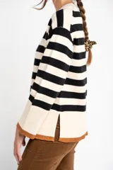 Sweater de punto con diseño a rayas horizontales en color negro y crema, de corte oversize. Presenta cuello redondo, mangas largas con puños acanalados y un detalle de borde inferior en color cobre con acabado brillante.