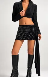 Conjunto de dos piezas compuesto por un blazer corto tipo torera de manga larga y una minifalda ajustada con detalle de strass brillante. La falda presenta un diseño drapeado y la chaqueta tiene un corte estructurado.