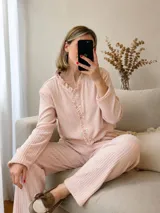 Conjunto de pijama compuesto por una remera de manga larga con botones frontales y detalle de volados en el cuello y la solapa, y un pantalón de corte recto y holgado. Ambas piezas están confeccionadas en tejido morley suave y elástico.
