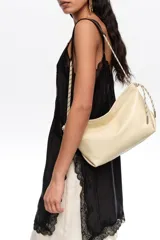 Bolso de hombro mediano de piel color beige, con cierre de cremallera, asas de cordón ajustable y logo grabado en el frente.