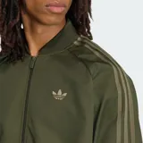 Campera Adidas modelo SST TT color verde militar, con cierre frontal, cuello alto y las clásicas tres tiras de la marca en las mangas. Cuenta con el logo del trifolio bordado en el pecho.