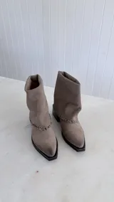 Bota de caña media confeccionada en cuero gamuzado color marrón oscuro, con diseño de caña arrugada y detalle de costura trenzada en la base. Cuenta con un taco cuadrado de madera y punta cuadrada.