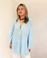 Blusa de broderie color celeste, de corte holgado, con escote en V y mangas largas. Presenta bordados calados en un patrón geométrico.