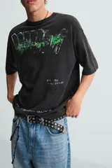 Camiseta boxy fit de punto tejido en hilatura de algodón, color negro con efecto lavado. Cuello redondo y manga corta. Estampado frontal con letras en blanco y verde.