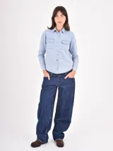Camisa de jean en tono celeste claro, con cuello clásico, cierre frontal con botones metálicos y dos bolsillos frontales con solapa.