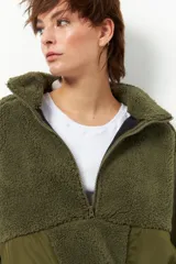 Buzo negro de teddy con cuello alto y cierre de cremallera parcial. Presenta bolsillos de nylon en la parte inferior delantera.