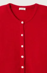 Cárdigan de punto rojo con cuello redondo, cierre frontal de botones y mangas largas con puños ajustados. Presenta un diseño de corte holgado y textura esponjosa.
