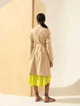Trench color beige de lino, largo hasta la rodilla, con lazo para ajustar en la cintura y cuello y solapa en lino color crudo. Cierre con botones de carey.