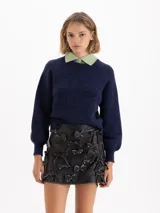 Mini falda de cuero ovino negro con efecto brush off, decorada con múltiples apliques de moños de cuero fijados con remaches metálicos. Posee bolsillos ojal en la parte trasera y forrería de acetato.