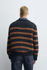 Jersey de punto con ajuste relajado, cuello redondo y manga larga. Presenta un diseño de rayas horizontales en color naranja sobre una base de color azul marino, con acabados en rib en puños, cuello y ruedo.