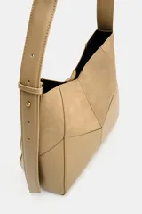 Bolso de hombro color tostado con diseño estructurado que combina paneles de cuero liso y gamuza con pespuntes visibles. Cuenta con un asa larga de hombro ajustable y cierre superior con botón imantado.