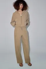 Pantalón de tiro medio color beige, de pierna ancha y corte recto. Cuenta con cintura elástica ajustable con cordones y bolsillos frontales.