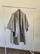 Ruana abierta con diseño estructurado y corte asimétrico, confeccionada en tela tipo tapiz con textura jaspeada en tonos grises.