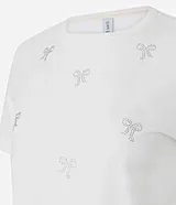Remera de algodón de corte clásico con cuello redondo y manga corta. Presenta un diseño estampado con pequeños lazos formados por aplicaciones de hotfix brillantes distribuidos por toda la prenda.