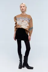 Sweater color camel de tejido de punto con cuello redondo y mangas largas. Presenta bordado de flor en el frente y la palabra 'Rebels' en la manga.
