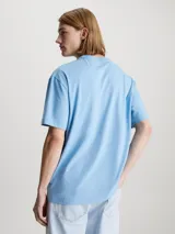 Remera de algodón en tono celeste claro, corte relajado y manga corta, con cuello redondo. Presenta un pequeño logo gráfico circular que simula un vinilo o disco en el lado izquierdo del pecho.