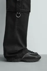 Zapatilla deportiva tipo running de color negro, confeccionada en una combinación de piezas de malla y material sintético. Presenta un diseño con cordonera curvada y una suela de volumen con diseño irregular.